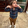 Calvin is registered to the contest to win money with this photo: toddler, child, indoor, kitchen, plaid_shirt, brown_pants, white_socks, socks_with_dog_face, sunglasses, standing, curious_expression, tile_floor, appliance, oven, cabinet, young_child, casual_clothing, cute, person, small_child