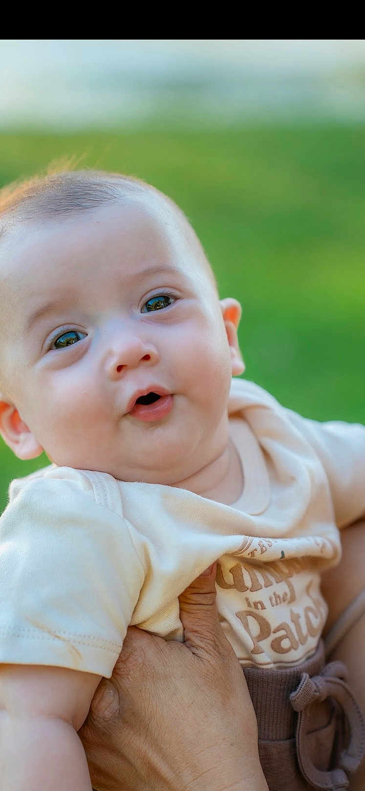 Jace is registered to the contest to win money with this photo: baby, infant, child, face, hand, clothing, outdoor, green_background, cute, portrait, skin, expression, holding, person, young, eyes, mouth, short_hair, toddler, shirt