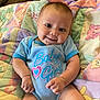 baby, infant, smiling, cute, onesie, blue_clothing, striped_clothing, face, child, happy, lying_down, quilt, blanket, colorful, animal_pattern, indoors, skin, person, young_child, cheerful