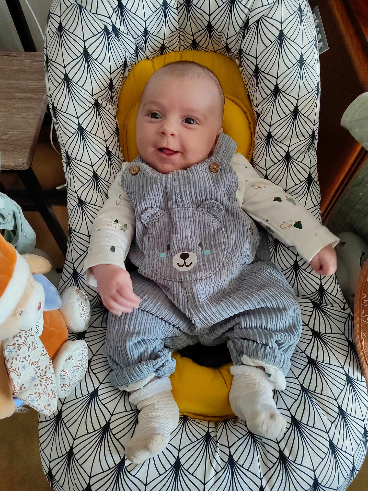 Charly participe au concours pour gagner de l'argent avec cette photo : baby, infant, child, smiling, baby_chair, overalls, socks, soft_toy, home_interior, patterned_fabric, yellow_cushion, cute_clothing, seated, happy, portrait, indoor, wooden_furniture, comfort, baby_girl, baby_boy