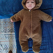 Charly participe au concours pour gagner de l'argent avec cette photo : baby, child, onesie, brown, fuzzy, hood, face, couch, blue, texture, footwear, boots, carpet, pattern, indoor, infant, cute, cozy, clothing, portrait