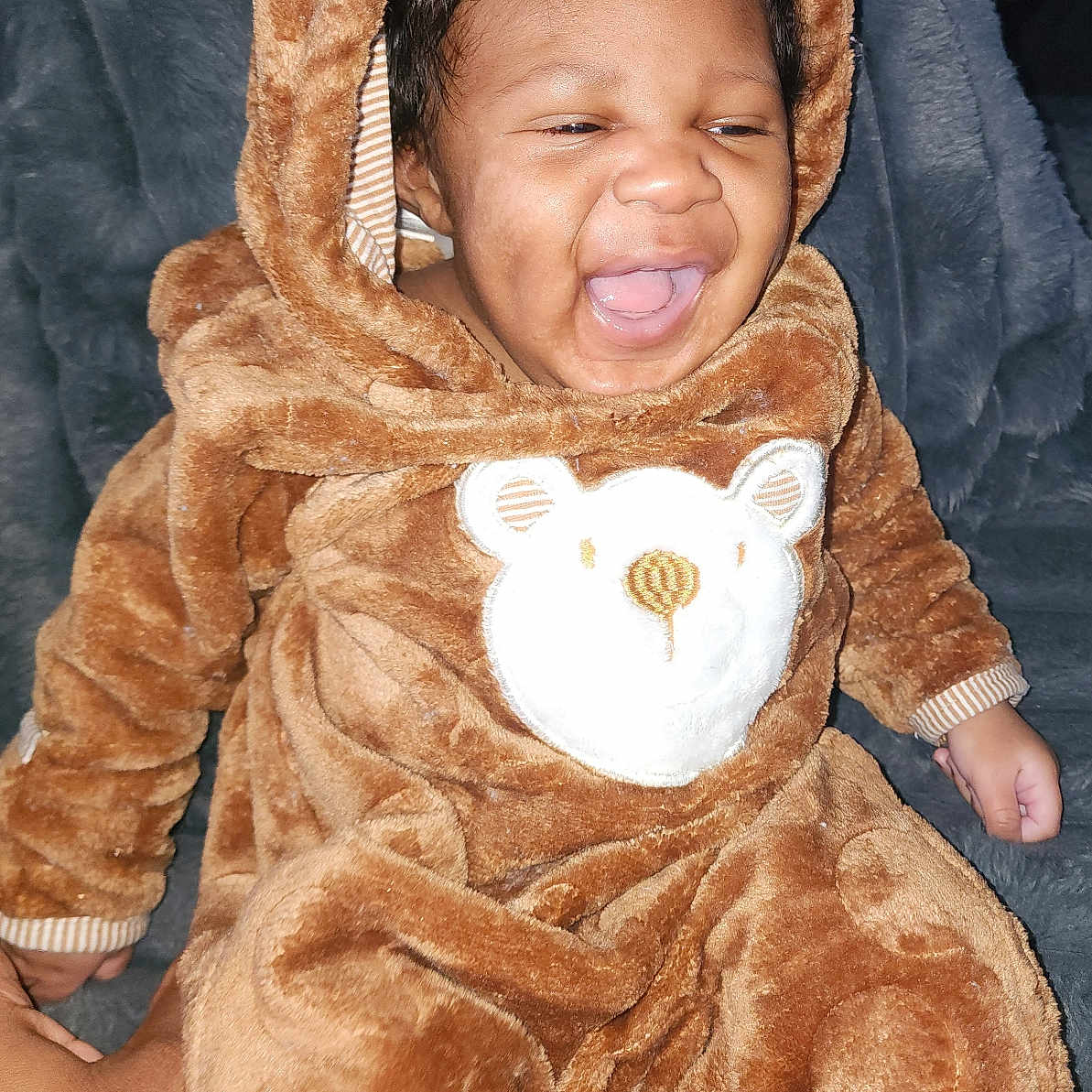 Phaylon is registered to the contest to win money with this photo: baby, child, infant, smiling, laughing, portrait, onesie, bear_costume, hood, plush, brown_clothing, sitting, indoor, blanket, close_up, face, happy, cute, phone_photography, watermark