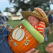 Madden joined the competition — help win amazing prizes! baby, sleeping, pumpkin, hat, straw_hat, orange, striped_clothing, child, outdoor, person, overalls, hand, grass, fall, autumn, costume, cute, festival, holding, portrait