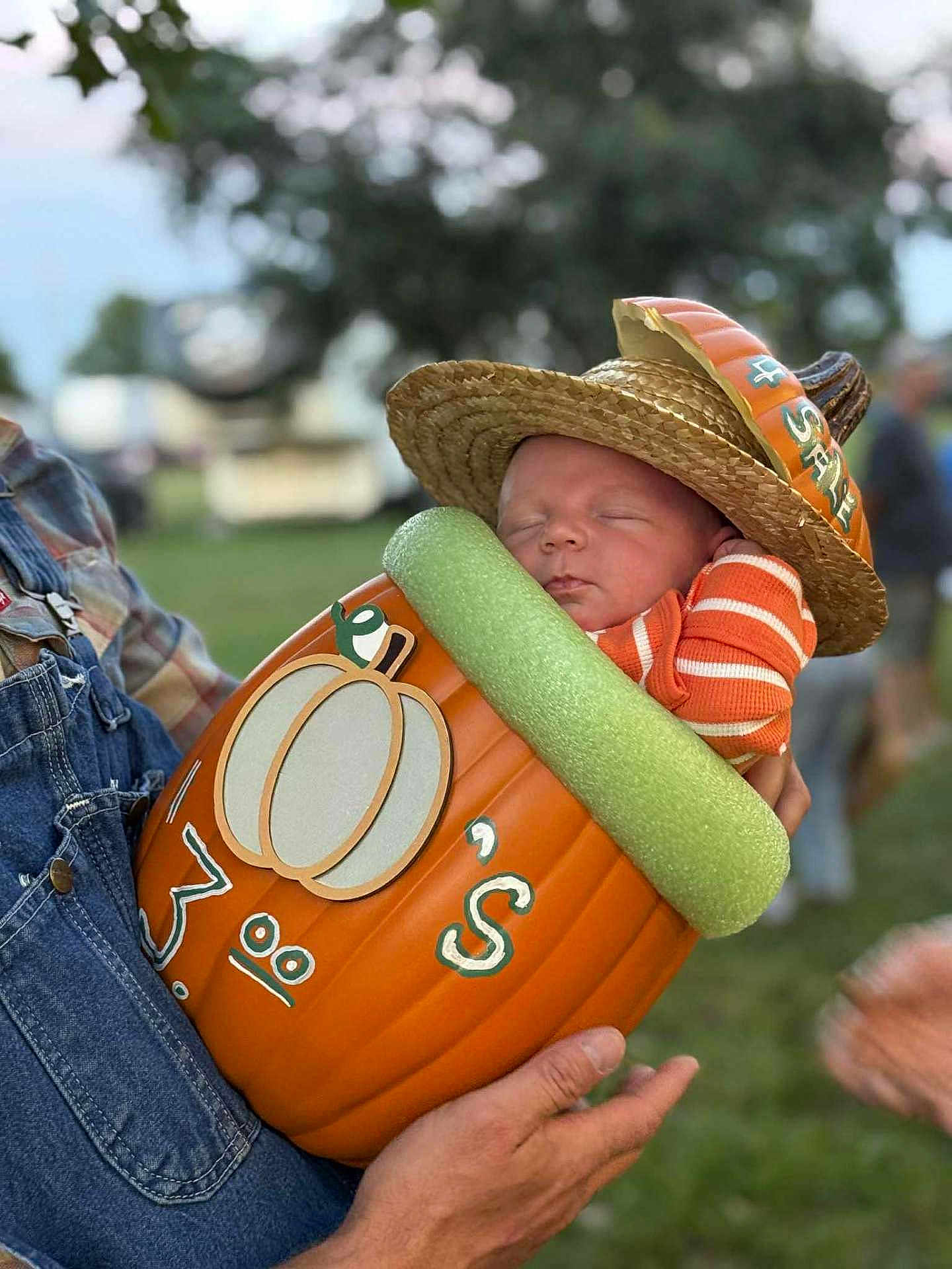 Madden joined the competition — help win amazing prizes! baby, sleeping, pumpkin, hat, straw_hat, orange, striped_clothing, child, outdoor, person, overalls, hand, grass, fall, autumn, costume, cute, festival, holding, portrait