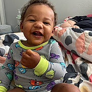 Kyrie is registered to the contest to win money with this photo: toddler, child, smiling, pajamas, bed, blanket, diaper, food, messy_face, indoor, person, happy, cute, sitting, infant, toy, patterned_clothing, hair, skin, room