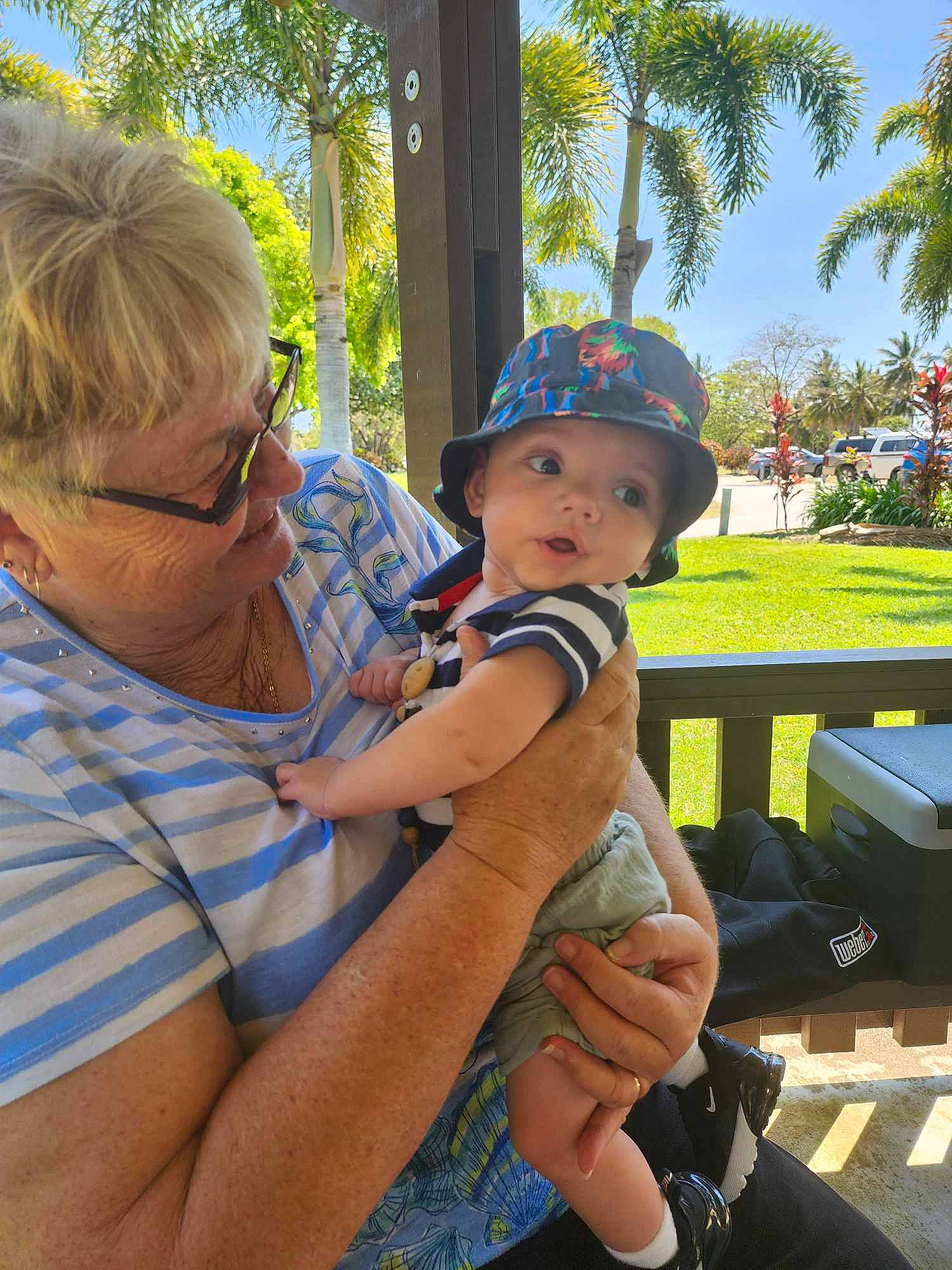 Max is registered to the contest to win money with this photo: baby, baseball_cap, child, event, fun, grass, happy, hat, headwear, leisure, palm_tree, person, plant, recreation, shorts, sitting, sky, summer, sun_hat, toddler