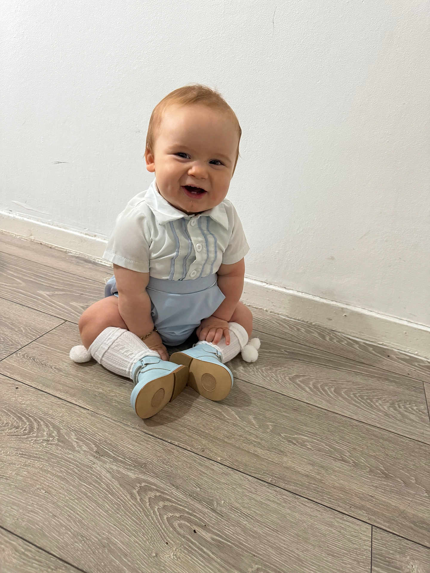 Christopher joined the competition — help win amazing prizes! baby, child, smiling, sitting, floor, white_wall, wooden_floor, blue_shorts, white_shirt, knee_socks, pom_poms, blue_shoes, happy, indoors, cute, portrait, person, infant, young_child, casual_clothing