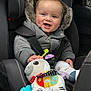 baby, child, car_seat, winter_jacket, fur_hood, plush_toy, zebra_toy, smiling, happy, infant, seatbelt, car_interior, cute, cozy, warm_clothing, child_safety, toy, hand, face, indoor