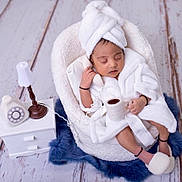 Aarav is registered to the contest to win money with this photo: newborn, baby, sleeping, white_robe, towel_turban, basket, cushion, blue_rug, floor, miniature_lamp, rotary_phone, small_table, indoor, cozy, cute, peaceful, infant, soft_texture, relaxing, portrait