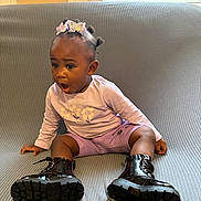 Skaila participe au concours pour gagner de l'argent avec cette photo : boots, butterfly_headband, child, couch, cute, expression, face, flower_print, footwear, grey_couch, hair_buns, indoors, long_sleeve_shirt, person, purple_clothing, shorts, sitting, surprised, toddler, young_child