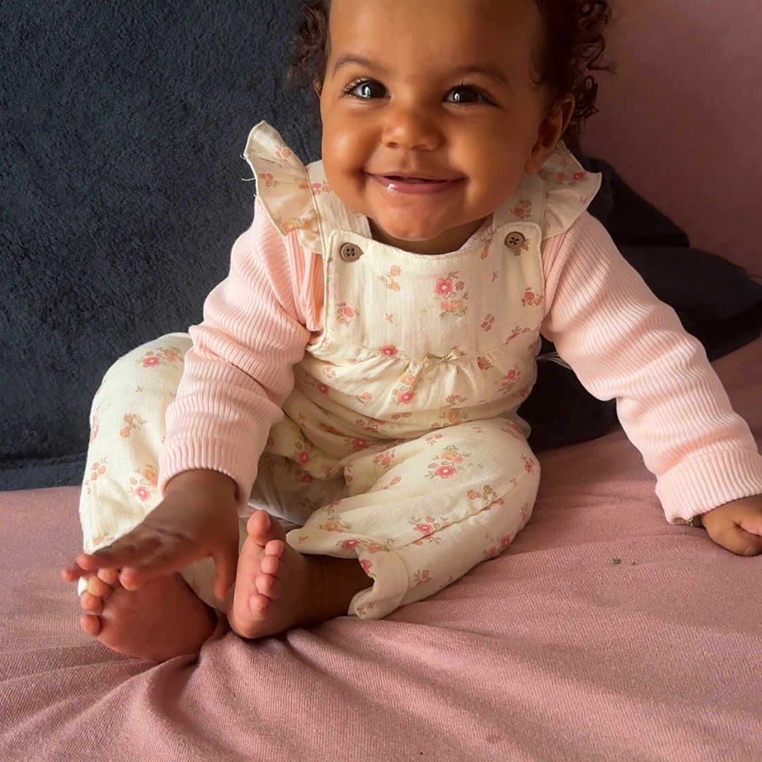 Keylah participe au concours pour gagner de l'argent avec cette photo : baby, blanket, child, cozy, curly_hair, cute, face, floral_overalls, foot, hand, happy, indoor, infant, pink_clothing, portrait, sitting, smile, soft_texture, toddler, young_child