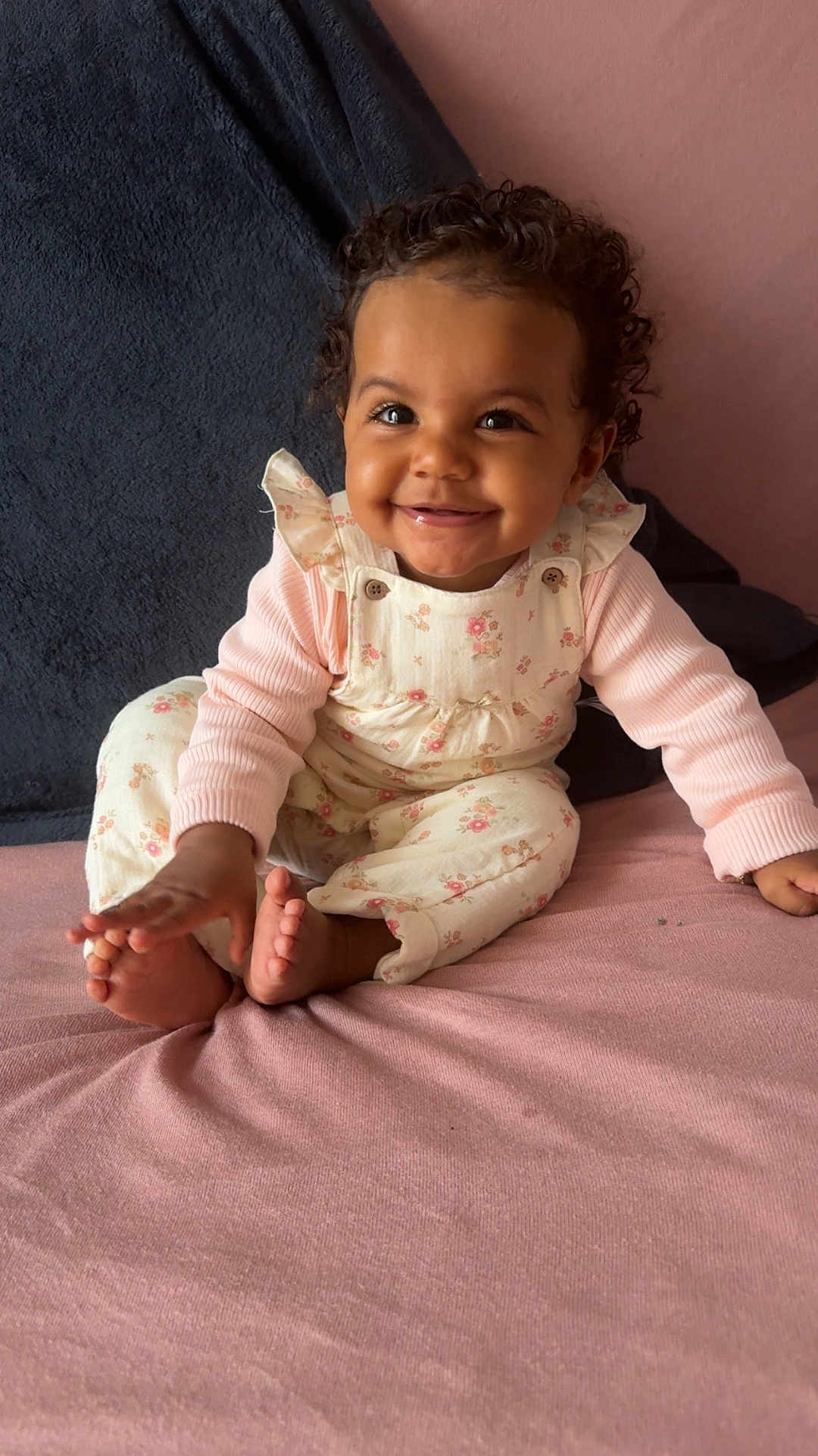 Keylah participe au concours pour gagner de l'argent avec cette photo : baby, child, smile, curly_hair, pink_clothing, floral_overalls, sitting, blanket, indoor, cute, happy, portrait, infant, toddler, hand, foot, face, cozy, soft_texture, young_child