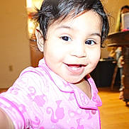 Analei is registered to the contest to win money with this photo: child, toddler, smile, pajamas, pink_clothing, face, indoors, home, wooden_floor, table, person, happy, cute, black_hair, bright, portrait, baby, closeup, young_child, joyful