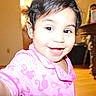 child, toddler, smile, pajamas, pink_clothing, face, indoors, home, wooden_floor, table, person, happy, cute, black_hair, bright, portrait, baby, closeup, young_child, joyful