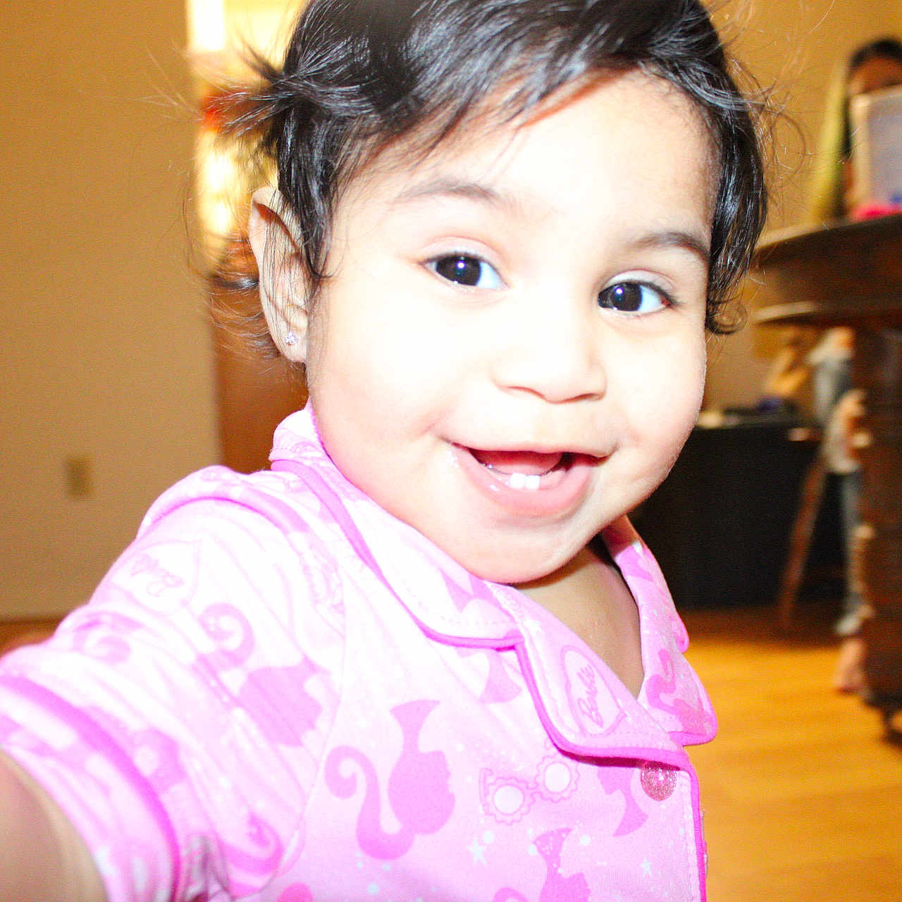 Analei is registered to the contest to win money with this photo: child, toddler, smile, pajamas, pink_clothing, face, indoors, home, wooden_floor, table, person, happy, cute, black_hair, bright, portrait, baby, closeup, young_child, joyful