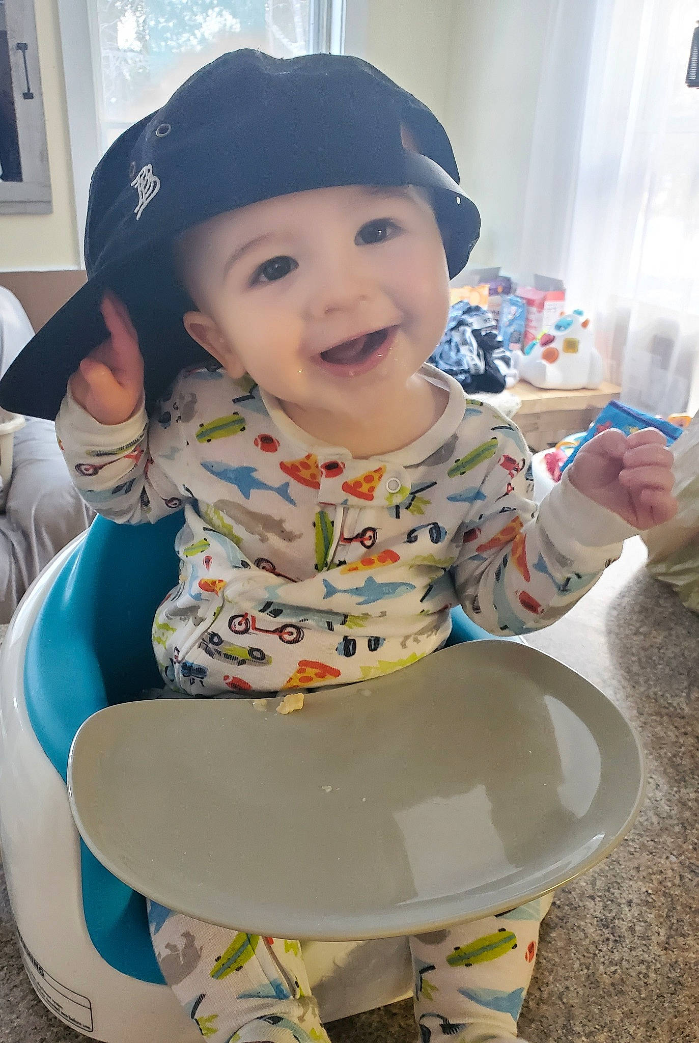 Ara is registered to the contest to win money with this photo: baby, baby_toddler_clothing, baseball_cap, bib, cap, chair, child, curtain, facial_expression, fashion_accessory, fun, happy, hat, headwear, pattern, person, picture_frame, play, sitting, sleeve