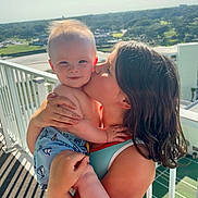 Hill is registered to the contest to win money with this photo: child, baby, kiss, balcony, sunlight, outdoor, smile, happy, person, holding, hair, clothing, skin, daytime, railing, nature, scenery, summer, affection, love
