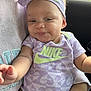 baby, infant, child, person, clothing, purple, headband, nike, onesie, smiling, arm, car_interior, seat, cute, face, hand, sitting, apparel, young, happy