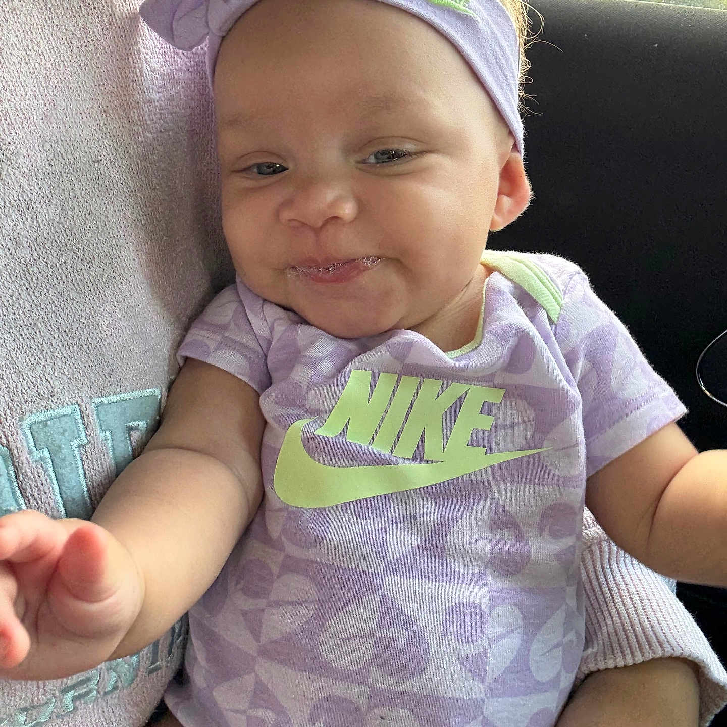 Harlowe is registered to the contest to win money with this photo: apparel, arm, baby, car_interior, child, clothing, cute, face, hand, happy, headband, infant, nike, onesie, person, purple, seat, sitting, smiling, young