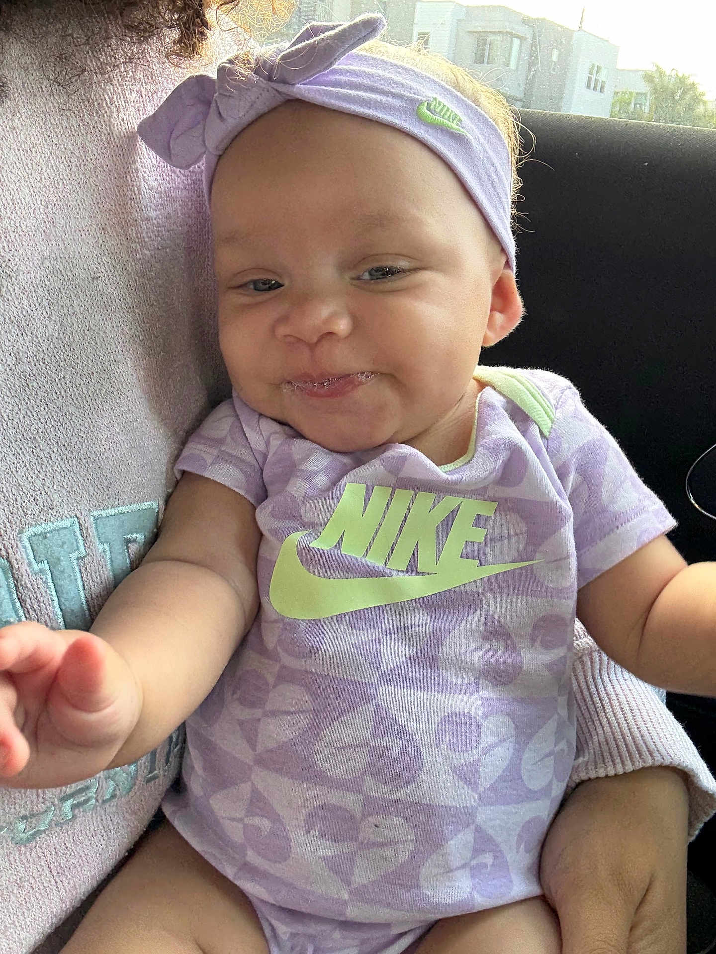 Harlowe is registered to the contest to win money with this photo: baby, infant, child, person, clothing, purple, headband, nike, onesie, smiling, arm, car_interior, seat, cute, face, hand, sitting, apparel, young, happy