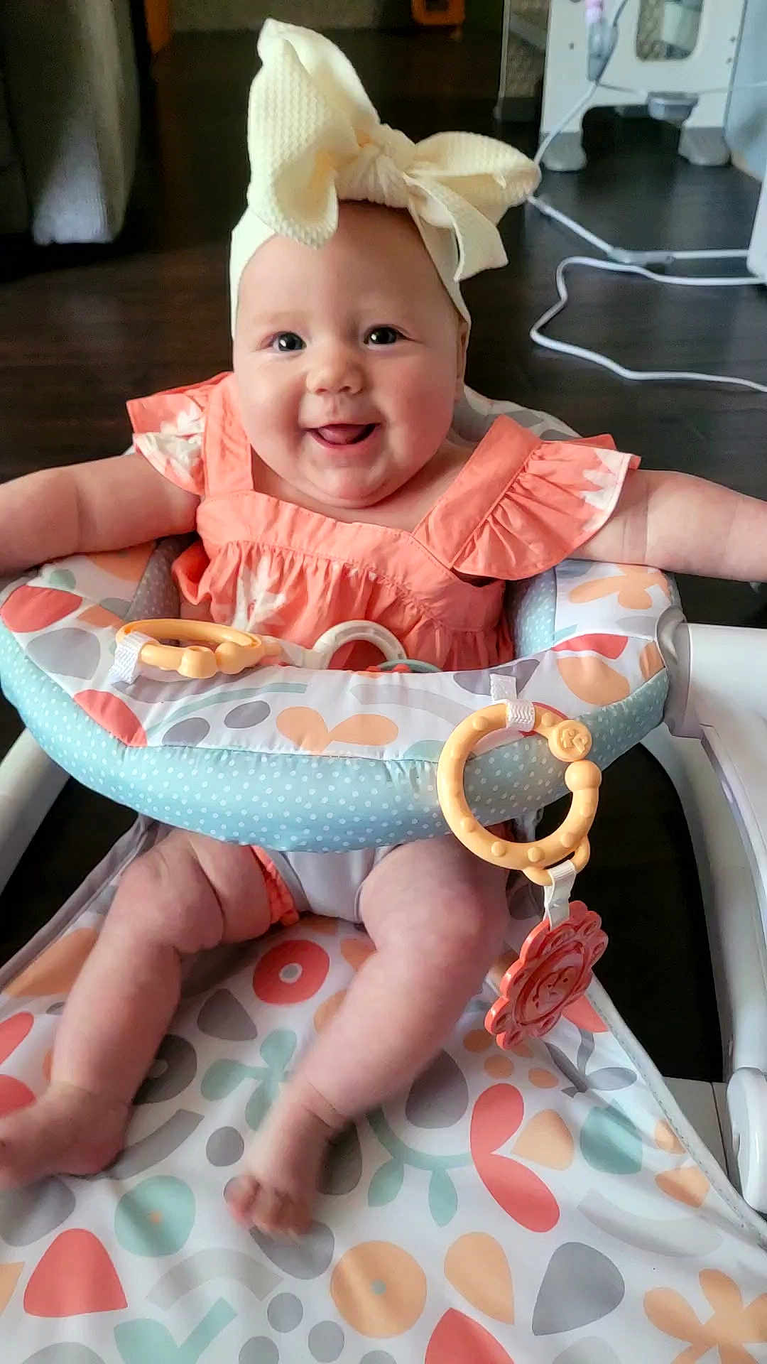 Zoee joined the competition — help win amazing prizes! baby, child, infant, smiling, bow, headwear, baby_seat, toy, colorful, patterned, happy, cute, indoor, floor, clothing, pink_dress, legs, arms, face, person