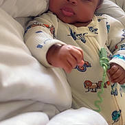 Marlon Shaw Jr is registered to the contest to win money with this photo: baby, infant, blanket, onesie, hand, face, cozy, cute, indoors, bed, sleepwear, child, peaceful, soft, portrait, person, lying_down, young, warm, comfort