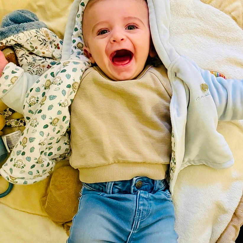 Léoh a rejoint le concours — aidez-le/la à gagner de superbes lots ! baby, blanket, child, clothing, cozy, cute, expression, face, happy, hooded_jacket, indoors, infant, jeans, joy, laying_down, smiling, socks, soft_toy, toddler, warm