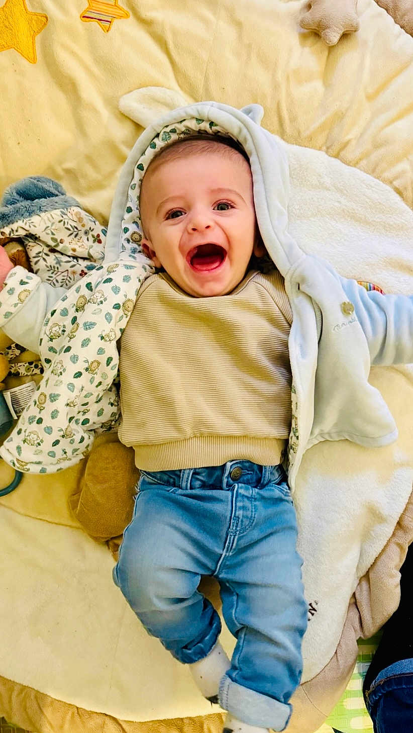 Léoh a rejoint le concours — aidez-le/la à gagner de superbes lots ! baby, child, smiling, happy, jeans, hooded_jacket, blanket, soft_toy, socks, infant, cute, laying_down, indoors, face, clothing, joy, expression, toddler, warm, cozy