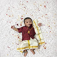 Shri Leonardo joined the competition — help win amazing prizes! baby, child, traditional_clothing, white_quilt, flower_petals, anklets, gold_necklace, curious, peaceful, indoors, portrait, infant, cute, lying_down, decorative, cultural, celebration, festive, small_hands, small_feet