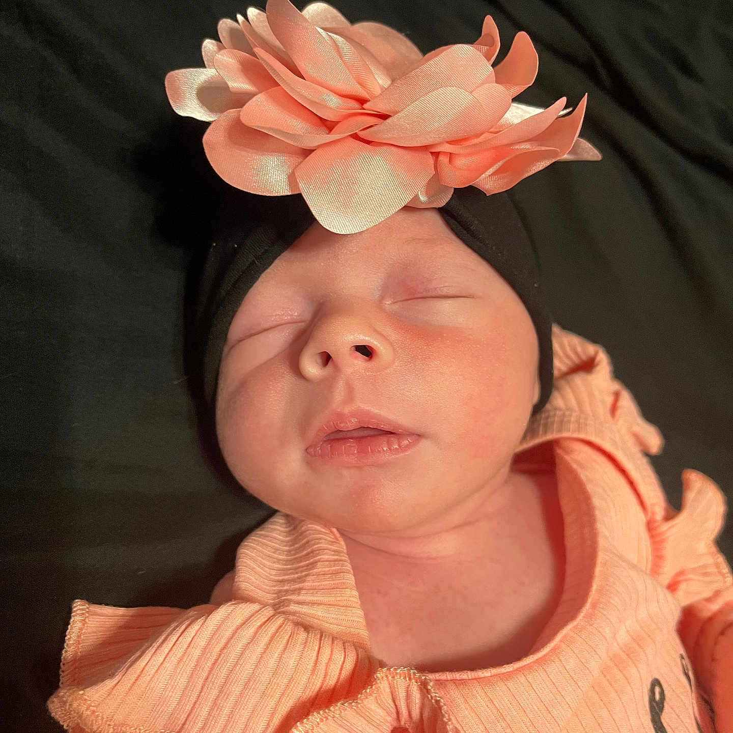 Hadley joined the competition — help win amazing prizes! apparel, baby, black_background, child, closeup, clothing, cute, fabric, face, flower, headband, infant, newborn, peaceful, peach, portrait, resting, ruffles, sleeping, soft_light