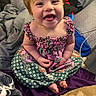 Bailey joined the competition — help win amazing prizes! baby, child, smiling, laughing, portrait, sitting, indoor, bed, blanket, floral_dress, colorful_clothing, patterned_fabric, brown_hair, blue_eyes, barefoot, infant, happy, home, cozy, photography