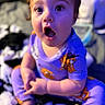 baby, child, infant, portrait, sitting, wide_eyes, open_mouth, surprised, indoor, pajamas, cartoon_clothing, colorful, purple_lighting, blue_lighting, close_up, face, hands, toys, blanket, home