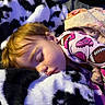 child, sleeping, toddler, portrait, face, blonde_hair, pajamas, blanket, plush_toy, stuffed_animal, bedtime, cozy, indoors, resting, lying_down, closed_eyes, soft_lighting, colorful_clothing, sports_pattern, comforter