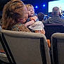 Tellisa is registered to the contest to win money with this photo: baby, woman, audience, indoor, event, seating, stage, lights, curly_hair, holding, back_of_head, clothing, people, chair, blurred_background, portrait, infant, fabric, love, family