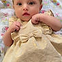 baby, infant, child, dress, golden_dress, bow, blanket, patterned_blanket, lying_down, cute, curious_eyes, small_hands, soft_skin, indoors, portrait, close_up, adorable, toddler, hair_tuft, expression