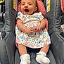 baby, infant, smiling, car_seat, dress, white_socks, happy, child, cute, indoor, person, seat, clothing, fabric, comfort, head, hands, legs, footwear, portrait