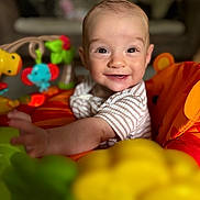 Mary joined the competition — help win amazing prizes! baby, child, smiling, indoor, toy, play_area, colorful, happy, infant, face, person, clothing, seat, bright_colors, portrait, cute, young_child, expression, baby_toy, living_room