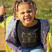 Lou-naya a rejoint le concours — aidez-le/la à gagner de superbes lots ! beads, black_shirt, blue_jeans, braided_hair, butterfly_print, casual_clothing, chain, child, face, floral_pattern, grin, hands, happy, outdoor, person, playground, seat, sunlight, swing, yellow_jacket