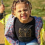 child, swing, braided_hair, beads, yellow_jacket, floral_pattern, black_shirt, butterfly_print, blue_jeans, outdoor, playground, sunlight, grin, face, hands, seat, chain, person, casual_clothing, happy