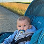 baby, child, stroller, pacifier, hoodie, outdoor, path, grass, wind_turbine, sky, daylight, nature, portrait, infant, seatbelt, toy, blue, teal, calm, cute