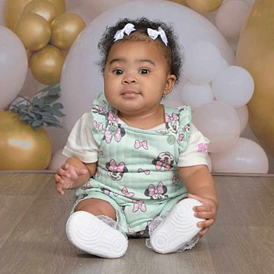 Layloni is registered to the contest to win money with this photo: toddler, child, baby, sitting, floor, balloons, gold_balloons, white_balloons, hair_bows, mint_green_outfit, cartoon_prints, curious_expression, indoor, portrait, cute, young_child, flooring, studio_photo, decor, infant