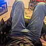 black_dog, book, carpet, casual, clothing, couch, dog, ear, face_part, floor, footwear, furniture, home, indoor, jeans, legs, living_room, person, relaxation, toy