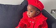 Mia is registered to the contest to win money with this photo: toddler, child, red_coat, beret, white_shoes, couch, grey_cushion, indoor, portrait, fashion, cute, sitting, young_child, curious, clothing, footwear, furniture, home, cozy, casual