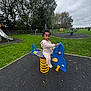 toddler, child, playground, spring_rider, blue, dolphin, outdoor, grass, trees, slide, fence, cloudy_sky, park, play_equipment, casual_clothing, fun, young_child, person, daytime, nature