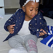 Mia is registered to the contest to win money with this photo: toddler, child, sitting, jacket, heart_pattern, headband, bow, curly_hair, white_shoes, leggings, indoor, mattress, cute, casual_clothing, small_hand, footwear, portrait, young_child, curious, baby