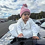 car, child, cloudy_sky, curious, cute, daylight, dress, hat, hood, outdoor, parking_lot, person, pink_hat, portrait, reflection, toddler, trees, white_clothing, white_shoes, winter_clothing