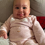 Halya participe au concours pour gagner de l'argent avec cette photo : baby, child, smiling, tongue_out, onesie, pink_outfit, couch, cushion, pillow, indoor, portrait, sitting, face, hand, legs, cozy, fabric, home_interior, cute, photography