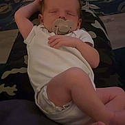 Jenson is registered to the contest to win money with this photo: baby, sleeping, pacifier, white_onesie, infant, resting, couch, cushion, hand, foot, person, indoor, comfort, relaxation, child, human, portrait, peaceful, nap, soft_lighting