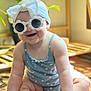 baby, child, sunglasses, headband, bow, smile, indoor, plant, wooden_floor, cute, blue_outfit, polka_dots, happy, sitting, infant, sunlight, portrait, fashion, accessory, baby_fashion