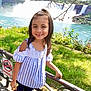 blue_clothing, child, daylight, girl, grass, greenery, happy, nature, outdoor, person, portrait, railing, scenic, smiling, striped, summer, sunlight, tourist_spot, water, waterfall